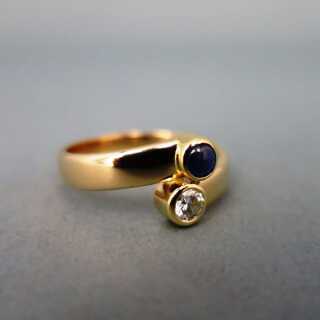 Woman gold bypass ring with sparkly diamond and blue sapphire cabochon